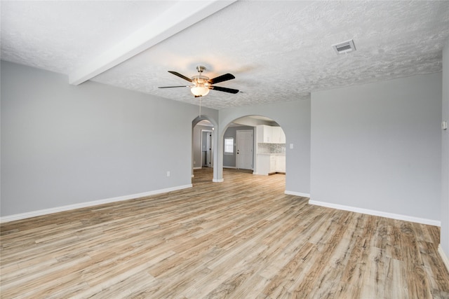 unfurnished room with baseboards, arched walkways, ceiling fan, a textured ceiling, and light wood-type flooring