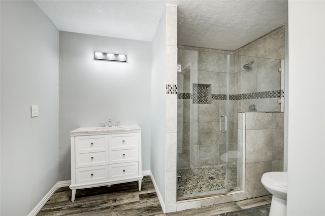 bathroom with toilet, wood finished floors, a shower stall, baseboards, and vanity