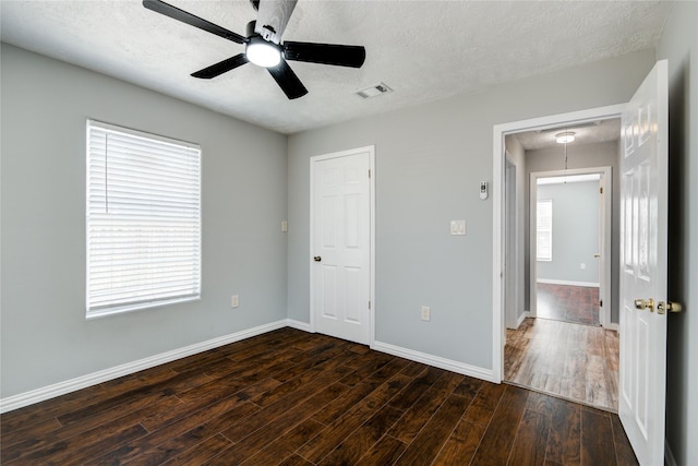 unfurnished bedroom featuring visible vents, baseboards, dark wood finished floors, a textured ceiling, and a ceiling fan