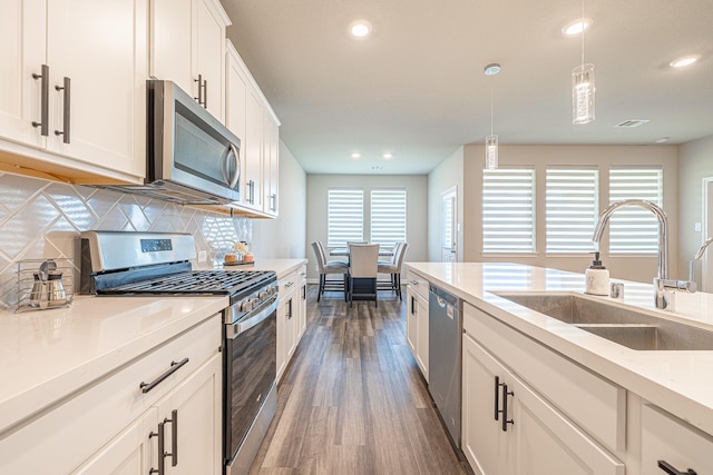 kitchen with dark wood-type flooring, decorative backsplash, appliances with stainless steel finishes, hanging light fixtures, and a sink