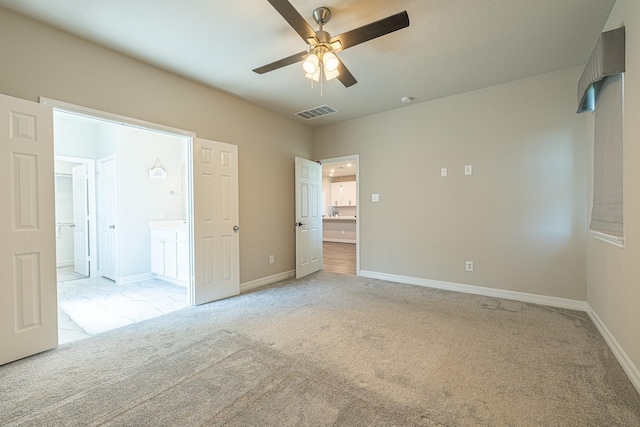 unfurnished bedroom with visible vents, connected bathroom, a walk in closet, baseboards, and light carpet