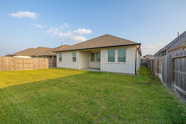 rear view of property featuring brick siding, a fenced backyard, a lawn, and a patio area