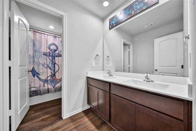 bathroom with a sink, visible vents, wood finished floors, and double vanity