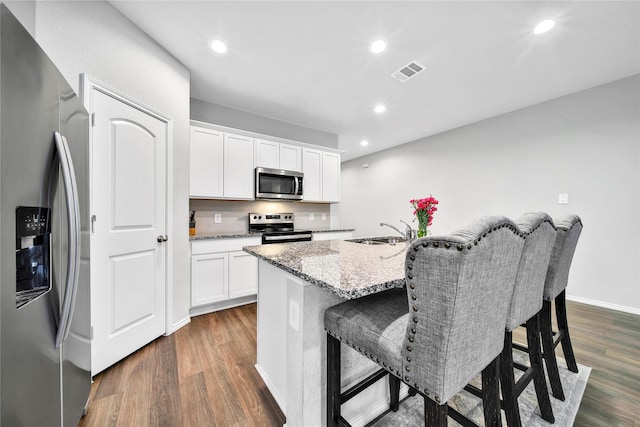 kitchen with visible vents, light stone countertops, dark wood finished floors, stainless steel appliances, and a sink