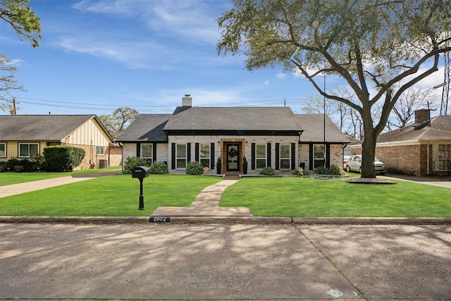 view of front of home featuring a front yard, brick siding, and a chimney