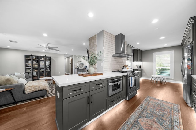 kitchen featuring dark wood-style flooring, stainless steel appliances, light countertops, wall chimney range hood, and backsplash