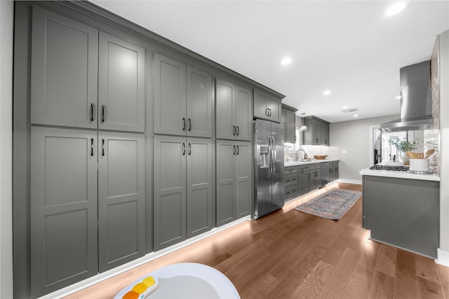 kitchen with wood finished floors, a sink, decorative backsplash, wall chimney range hood, and stainless steel fridge