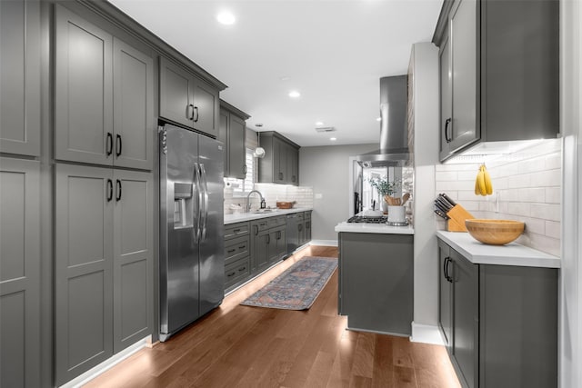 kitchen with dark wood-type flooring, wall chimney range hood, stainless steel fridge with ice dispenser, and light countertops