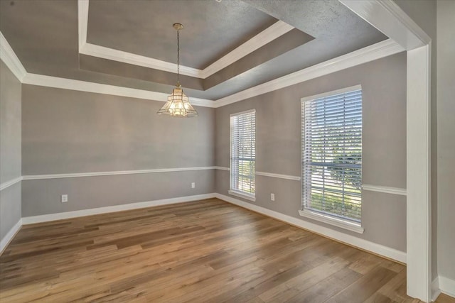 empty room with a tray ceiling, crown molding, wood finished floors, and baseboards