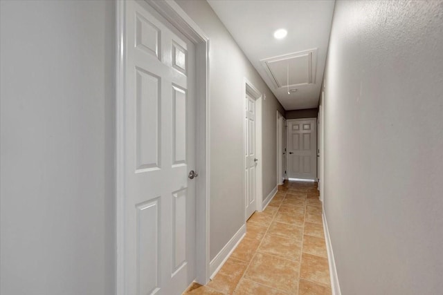 corridor featuring baseboards, attic access, and light tile patterned flooring