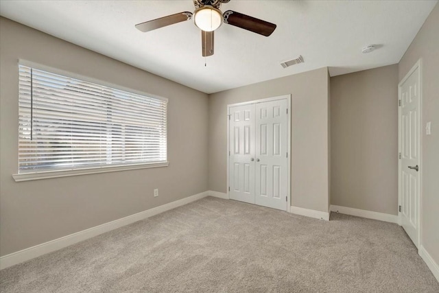 unfurnished bedroom featuring visible vents, baseboards, light colored carpet, a closet, and a ceiling fan