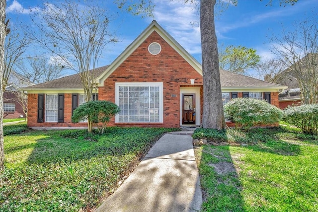 view of front of property with a front yard, brick siding, and a shingled roof