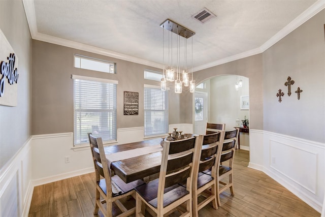 dining space featuring visible vents, arched walkways, ornamental molding, light wood-style floors, and wainscoting