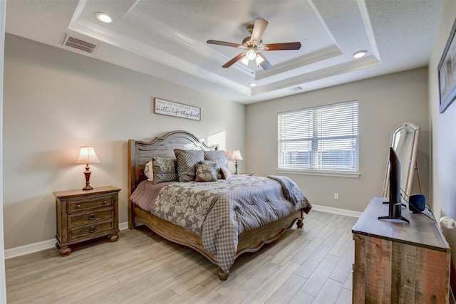 bedroom featuring visible vents, a raised ceiling, light wood-style floors, and baseboards