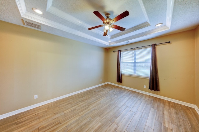 spare room with a textured ceiling, visible vents, light wood-style flooring, and a raised ceiling