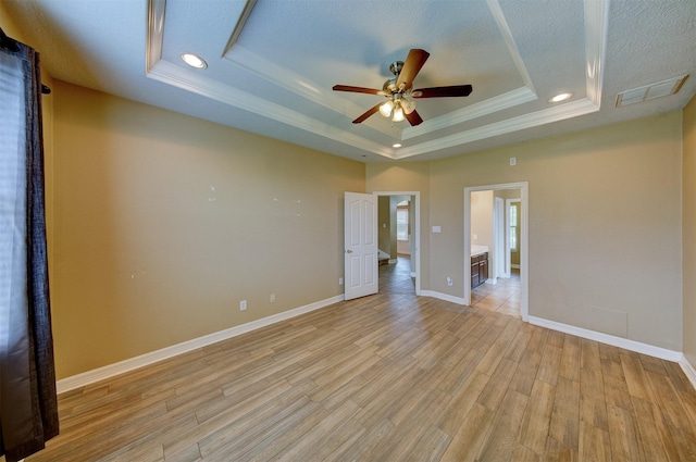 empty room with a tray ceiling, visible vents, light wood-style flooring, and ceiling fan