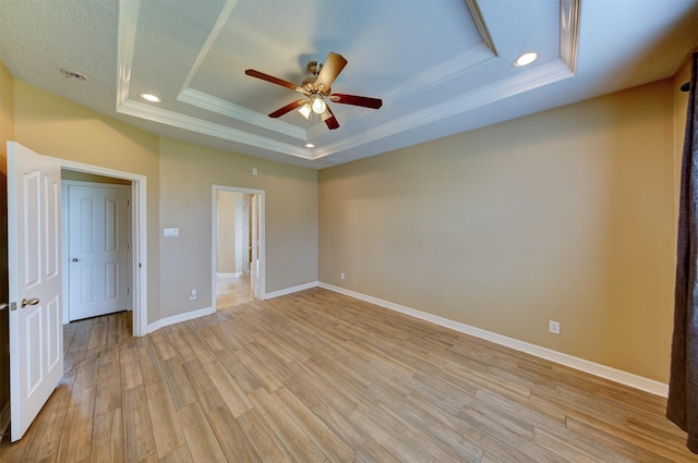 spare room with a tray ceiling, ornamental molding, baseboards, light wood finished floors, and a ceiling fan