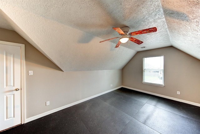 additional living space with a ceiling fan, a dark floor, baseboards, and a textured ceiling