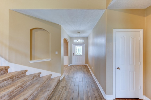 entrance foyer featuring stairs, arched walkways, wood finished floors, and a textured ceiling