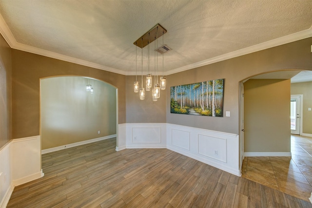 empty room featuring arched walkways, a wainscoted wall, a textured ceiling, and wood finished floors