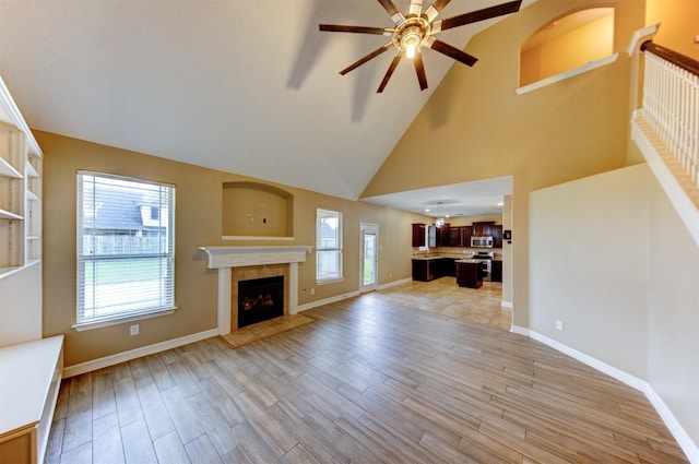 unfurnished living room featuring ceiling fan, a tile fireplace, light wood-style floors, and a wealth of natural light