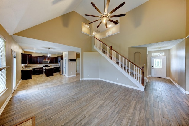 unfurnished living room with light wood-style flooring, stairs, baseboards, a sink, and a ceiling fan