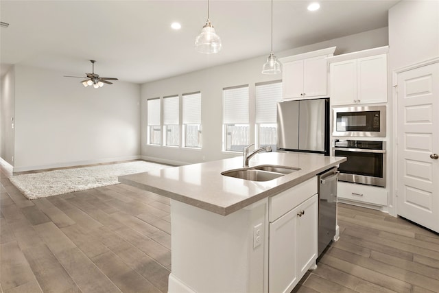 kitchen featuring light wood-style flooring, appliances with stainless steel finishes, white cabinetry, a ceiling fan, and a sink