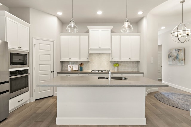 kitchen with a sink, backsplash, wood finished floors, stainless steel appliances, and a kitchen island with sink