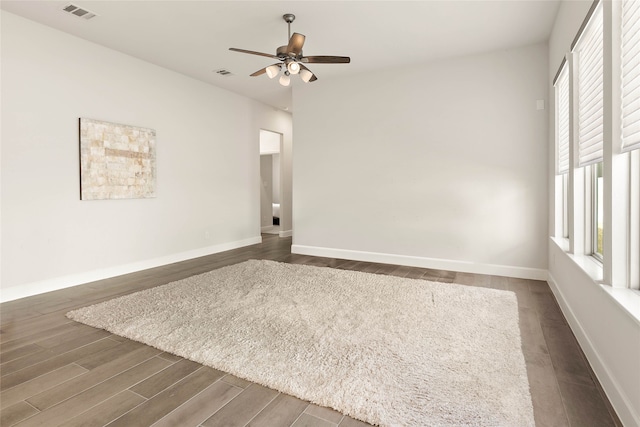 unfurnished room featuring dark wood-style floors, visible vents, baseboards, and a ceiling fan