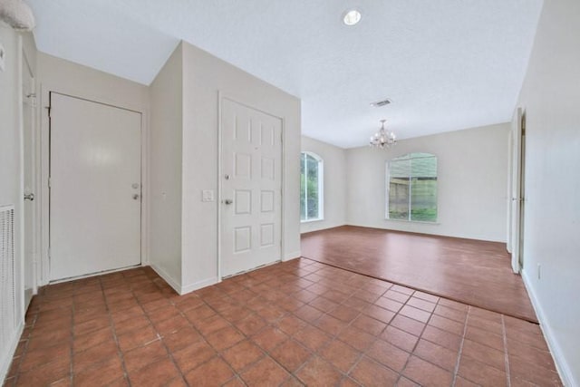 tiled entrance foyer with a textured ceiling, baseboards, and a chandelier