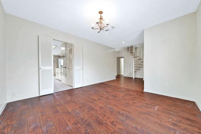 unfurnished living room with a chandelier, stairway, baseboards, and hardwood / wood-style flooring