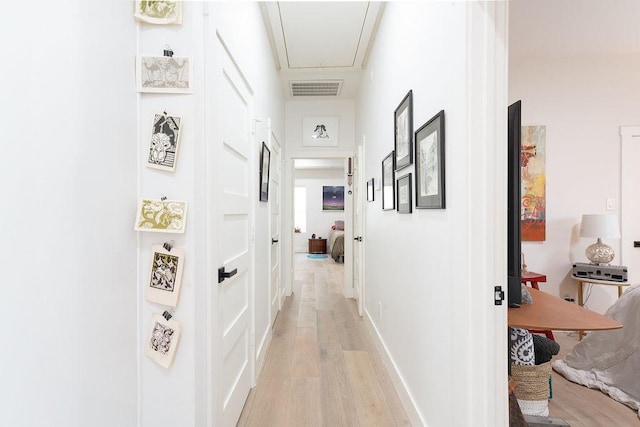 hallway with visible vents, baseboards, attic access, and light wood finished floors