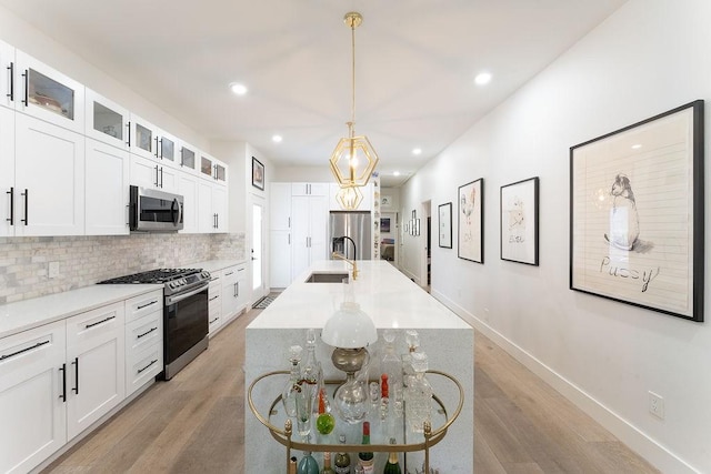 kitchen with baseboards, an island with sink, stainless steel appliances, light wood-style floors, and tasteful backsplash