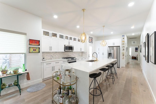 kitchen with backsplash, a breakfast bar area, light wood-style flooring, appliances with stainless steel finishes, and a sink