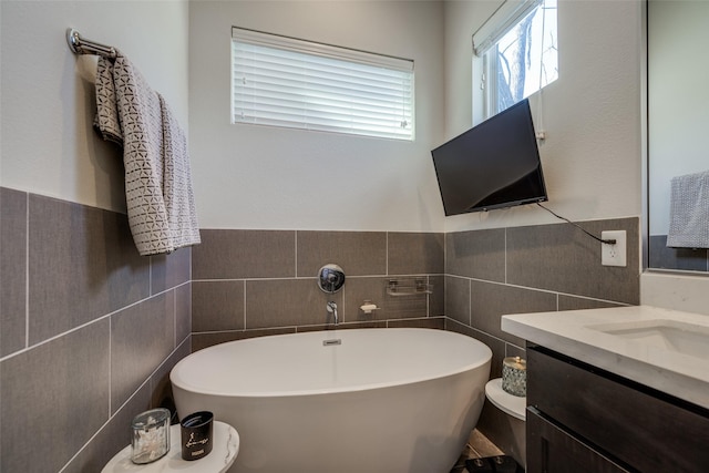 full bath featuring wainscoting, vanity, tile walls, and a freestanding tub