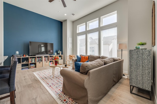 living room with visible vents, a ceiling fan, wood finished floors, a high ceiling, and baseboards