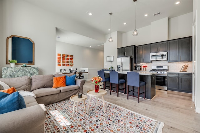 living room featuring recessed lighting, visible vents, light wood-style flooring, and a high ceiling