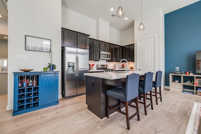 kitchen featuring light wood finished floors, a kitchen breakfast bar, appliances with stainless steel finishes, a towering ceiling, and a sink