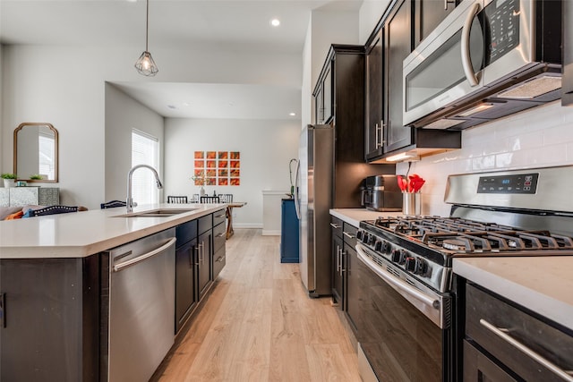 kitchen featuring backsplash, light countertops, light wood-style floors, stainless steel appliances, and a sink