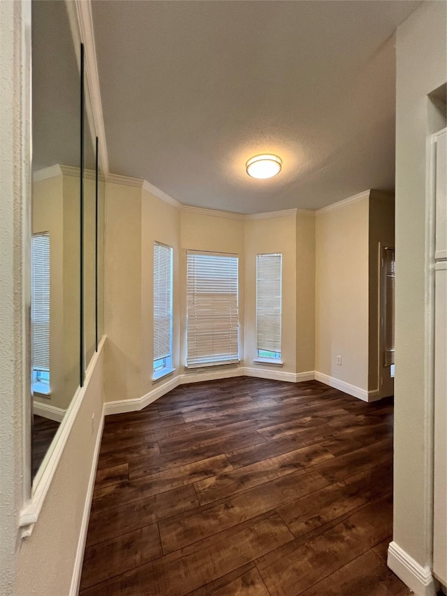 empty room with dark wood finished floors, crown molding, and baseboards