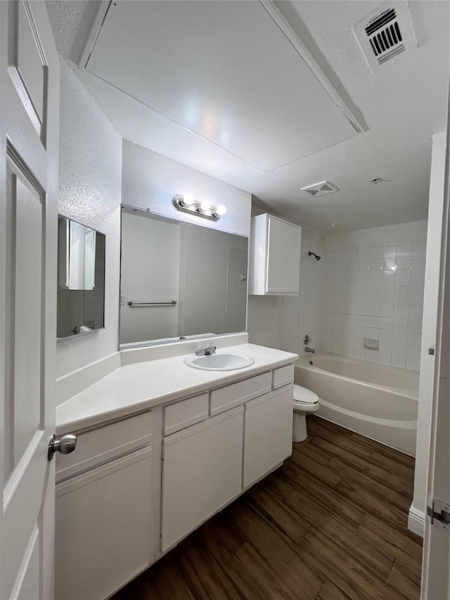 bathroom with visible vents, toilet, wood finished floors,  shower combination, and vanity