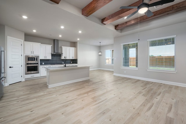 kitchen featuring wall chimney range hood, beamed ceiling, decorative backsplash, light wood-style flooring, and appliances with stainless steel finishes