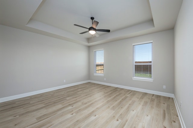 empty room with ceiling fan, baseboards, light wood-style floors, and a tray ceiling