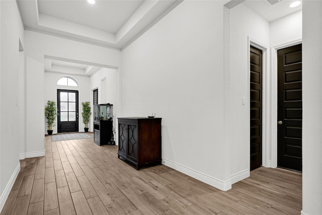 foyer with a raised ceiling, light wood-style flooring, recessed lighting, and baseboards