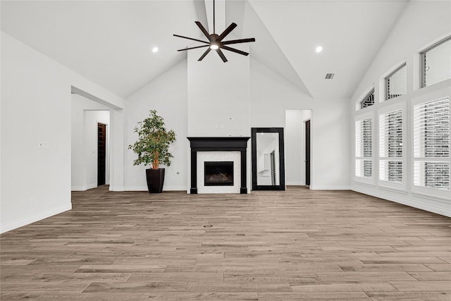 unfurnished living room featuring a fireplace, high vaulted ceiling, light wood-type flooring, and ceiling fan