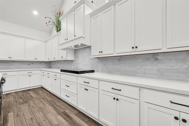 kitchen with backsplash, premium range hood, wood finished floors, white cabinets, and black electric cooktop