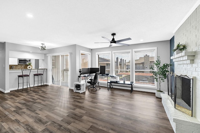 living room with a brick fireplace, baseboards, ceiling fan, wood finished floors, and a textured ceiling