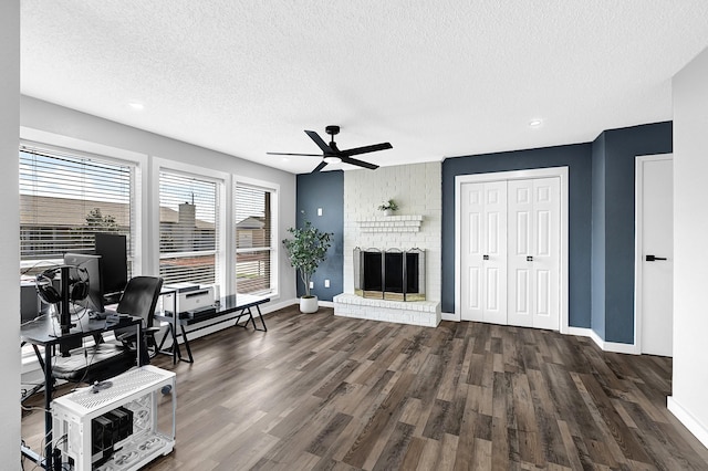 home office featuring a brick fireplace, baseboards, ceiling fan, dark wood-style floors, and a textured ceiling