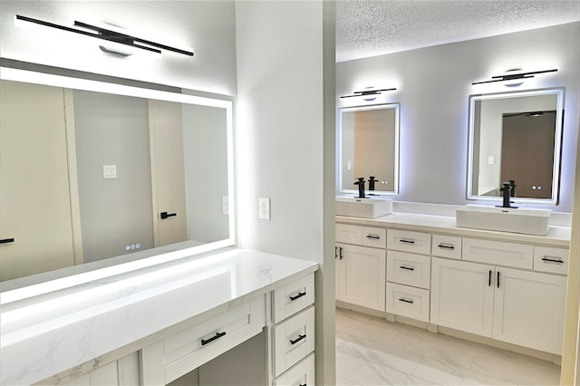 bathroom featuring a sink, a textured ceiling, marble finish floor, and double vanity