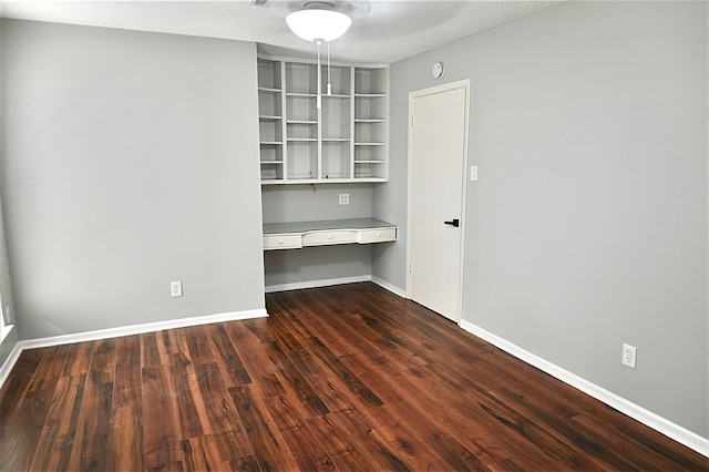 spare room featuring baseboards, built in desk, dark wood-style flooring, and a textured ceiling